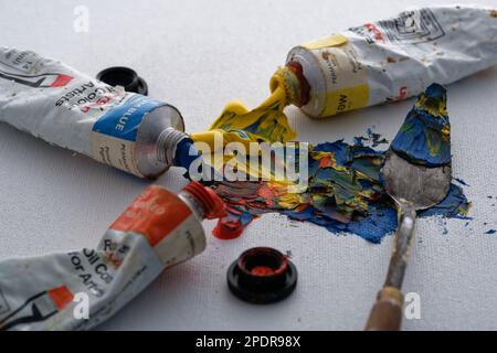 Pitture a olio colorate e un coltello a palette tutti mescolati su uno sfondo di cartone di tela. Blu, rosso e giallo per creare una foto. Il processo creativo. Foto Stock