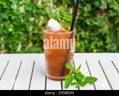 Tè verde ghiaccio con lychee e menta su tavolo di legno bianco contro foglie verdi con spazio copia Foto Stock