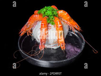 Cinque gamberetti arancioni all'interno della noce di cocco con salsa isolata su sfondo nero vista laterale Foto Stock