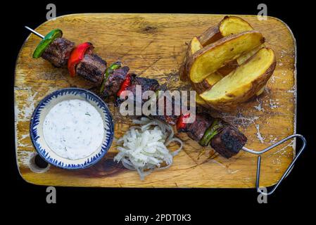 Spiedini di maiale serviti con insalata e salsa su sfondo nero vista dall'alto Foto Stock