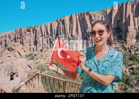 Ragazza felice con bandiera nazionale turca con la famosa valle di Ihlara in Cappadocia sullo sfondo. Destinazioni turistiche e di viaggio a Turkiye Foto Stock