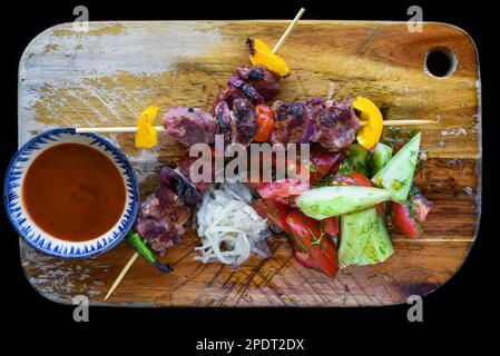 Spiedini di maiale serviti con insalata e salsa su sfondo nero vista dall'alto Foto Stock