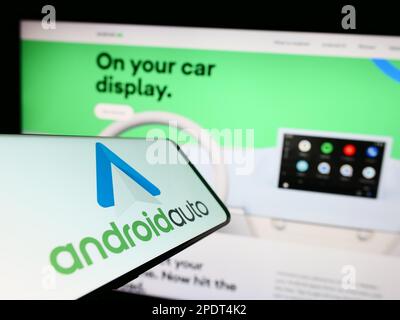 Cellulare con logo di app mobile Android Auto (Google) sullo schermo di fronte al sito web. Messa a fuoco al centro a destra del display del telefono. Foto Stock