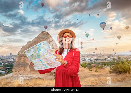 Un turista femminile determinato con una mappa in mano guarda ai mongolfiere sbalorditivi in Cappadocia. Foto Stock