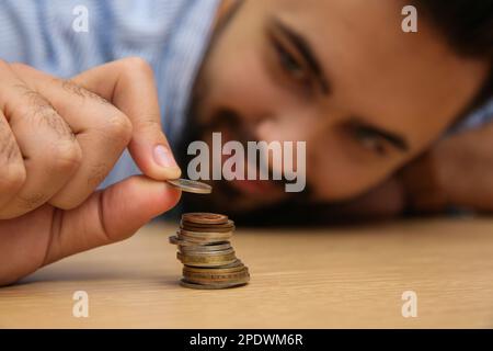 Uomo impilando monete a tavola di legno, fuoco a portata di mano. Risparmio di denaro Foto Stock