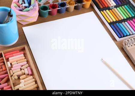 Foglio bianco di carta, pastelli colorati di gesso e altri strumenti di disegno su tavola di legno. Luogo di lavoro dell'artista moderno Foto Stock