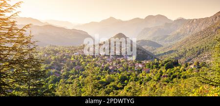 ambiente tranquillo e sereno del villaggio, con le montagne che si innalzano sullo sfondo e la luce solare soffusa che proietta una calda luce soffusa sulla scena. Foto Stock