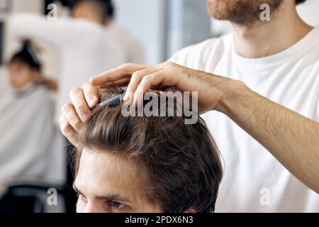 primo piano, professionale hairstylist maschile pettinare i capelli dei giovani clienti Foto Stock