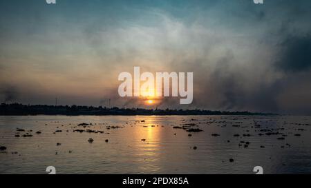 Il fumo campeggia dalle fornaci di mattoni come il sole sorge sopra il fiume Mekong con i suoi grumi di giacinto galleggiante di acqua a Long Xuyen nel delta del Mekong in Foto Stock