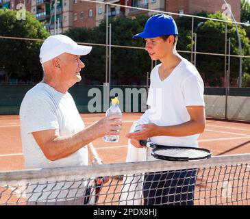 nonno e nipote parlano sul campo giocando a tennis Foto Stock