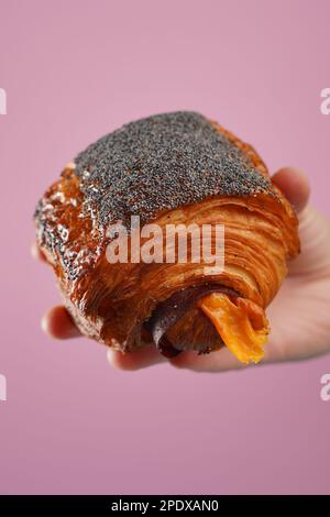 Croissant appena sfornato tenuto in mano su sfondo colorato Foto Stock