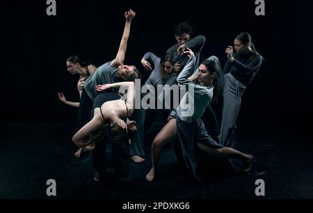 Auto-espressione attraverso i movimenti. Gruppo di giovani che ballano sullo sfondo nero dello studio. Concetto di danza contemporanea Foto Stock