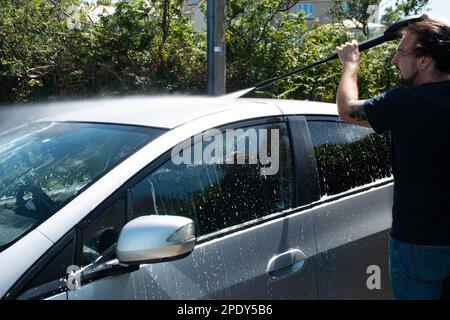 due morbillo per la pulizia di un'auto argentata spruzzando una schiuma con una idropulitrice per il lavaggio di un'auto Foto Stock