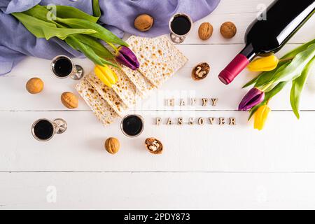 bicchieri d'argento con vino rosso, matzah, una bottiglia di vino e tulipani su fondo di legno bianco. lettere di legno Passover Foto Stock