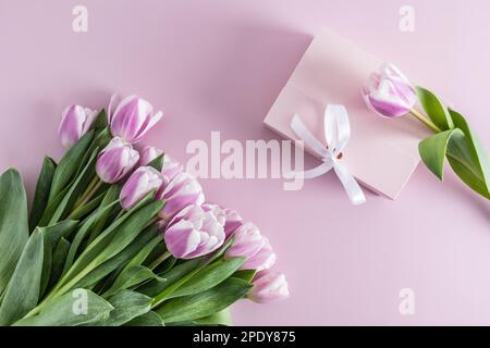 vista dall'alto di un grande bouquet di tulipani lilla e di una scatola di festa con un regalo. sfondo lilla Foto Stock