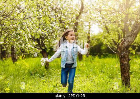 Una bella bambina attraversa un giardino fiorito in primavera. Cute bambino con capelli biondi in un giardino fiorente al tramonto Foto Stock