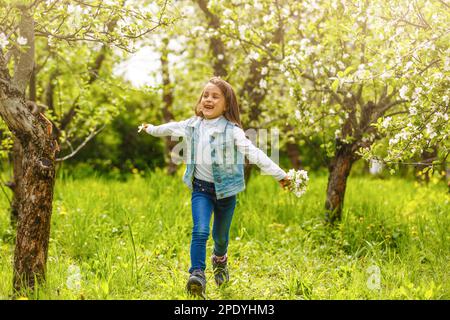 Una bella bambina attraversa un giardino fiorito in primavera. Cute bambino con capelli biondi in un giardino fiorente al tramonto Foto Stock