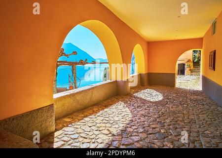Il luminoso porticato giallo sul lungolago del Lago di Lugano con vista su un lago e montagne, Oria, Valsolda, Italia Foto Stock