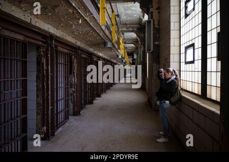 Giovane ragazza sorridente che visita e scatta foto nelle gallerie delle celle della prigione di Old Joliet Foto Stock