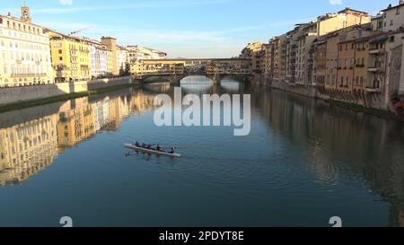 Il Ponte Vecchio, antico ponte ad arco segmentale con negozi e abitazioni sul fiume Arno, a Firenze. Riflessi dorati sull'acqua Foto Stock