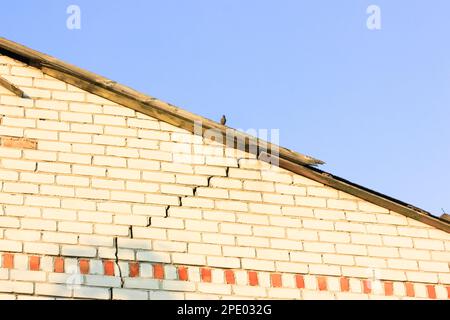 Una casa di mattoni bianchi a due piani con una crepa attraverso l'intera facciata contro un cielo blu. Esterno di un edificio residenziale in mattoni bianchi con tetto a capanna. Foto Stock