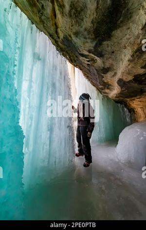 Karen Rentz esplorando dietro le tende formazione di ghiaccio utilizzato dagli arrampicatori di ghiaccio in Pictured Rocks National Lakeshore vicino a Munising, Upper Peninsula, Mah Foto Stock