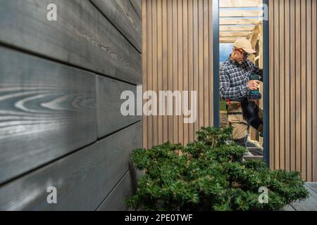 Moderno edificio personalizzato Garden Shed eseguito da Caucasian Construction Worker nel suo 40s. Installazione della finestra. Tema di architettura piccola. Foto Stock