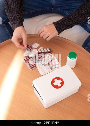 Alto angolo di raccolto maschio irriconoscibile in abiti casual seduto a tavolo di legno prendendo varie pillole posto vicino a scatola di aiuto medico a casa Foto Stock