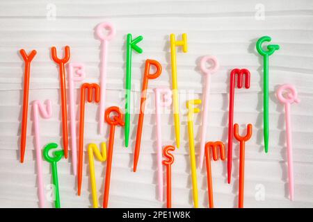 Bastoncini colorati in plastica con lettere inglesi in alto sparse sul bianco. Divertente giocattolo educativo per bambini che imparano l'alfabeto Foto Stock