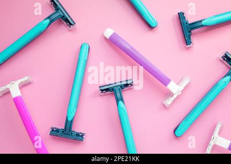 Molti rasoi monouso viola e blu su sfondo rosa. Colorful donna e uomo igiene accessori posa piatta Foto Stock