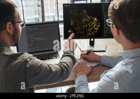 Primo piano di due specialisti di scienza dei dati maschili che lavorano insieme in ufficio, analizzando i big data sullo schermo. Codificatori che lavorano su un nuovo progetto Foto Stock