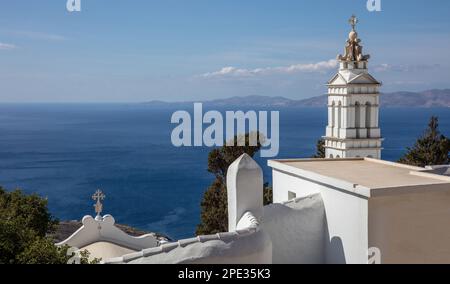 CICLADI, Grecia. Isola greca di Tinos, campanile della chiesa di Panagia, sul mare blu e sullo sfondo del cielo, paesaggio roccioso, giorno di sole Foto Stock