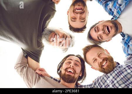 Un gruppo di amici maschi felici che si accoccolano, guardano la macchina fotografica, sorridono e ridono Foto Stock