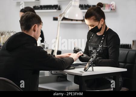Manicure maschile. Maestro di servizio unghie femminile che fa manicure per l'uomo adulto. Uomo seduto nel salone di bellezza Foto Stock