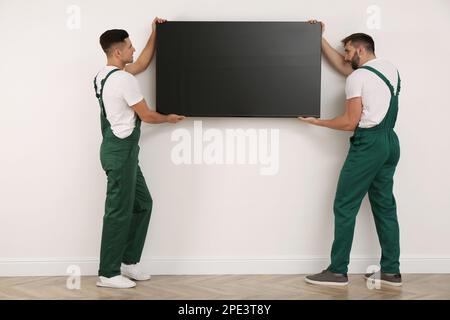 Tecnici professionisti che installano un moderno televisore a schermo piatto a parete al chiuso Foto Stock