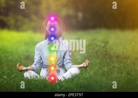 Giovane donna che medita sull'erba verde. Schema di sette chakra, illustrazione Foto Stock