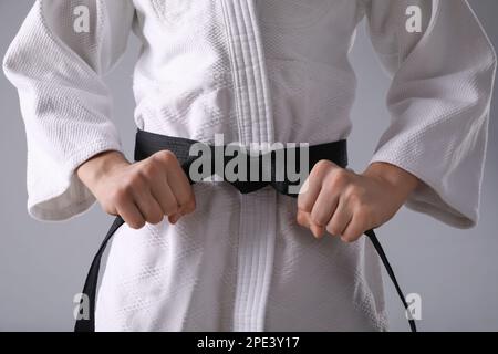 Maestro di arti marziali in keikogi con cintura nera su sfondo grigio, primo piano Foto Stock