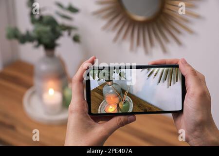 Donna che scatta foto di eleganti accessori interni su un tavolo di legno con smartphone, primo piano Foto Stock
