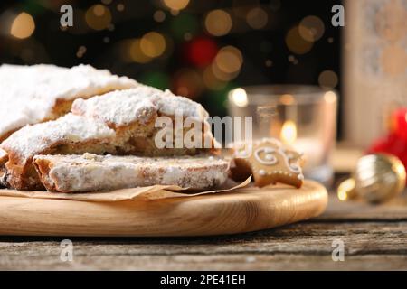 Tradizionale Stollen di Natale con zucchero a velo sulla tavola di legno contro sfocate luci festive Foto Stock