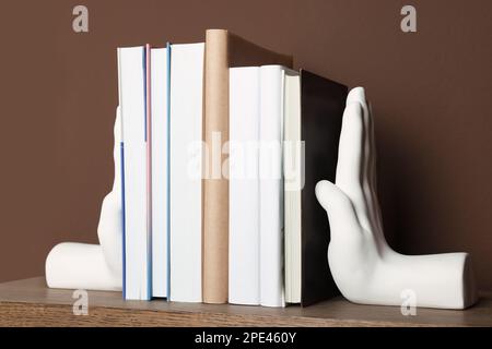 Bellissimi libri a forma di mano con libri su scaffale vicino a parete marrone Foto Stock