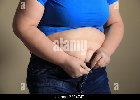 Donna sovrappeso cercando di buttare su jeans stretti su sfondo marrone chiaro, primo piano Foto Stock