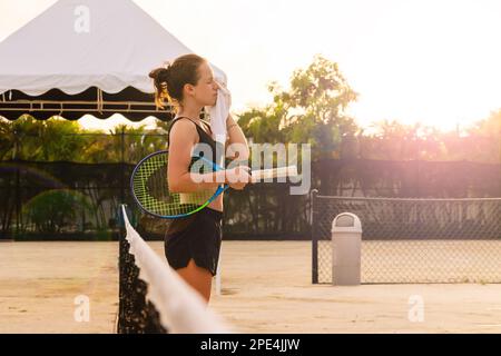 Donna atleta tennista strofinare il viso con un asciugamano mentre si trova in piedi sul campo da tennis. Foto Stock