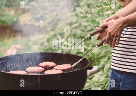 Il padre insegna al bambino a grigliare carne per hamburger alla griglia all'aperto Foto Stock