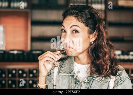 La ragazza annietta l'odore del vino e fa un volto con un'emozione di disgusto e dispiacere Foto Stock