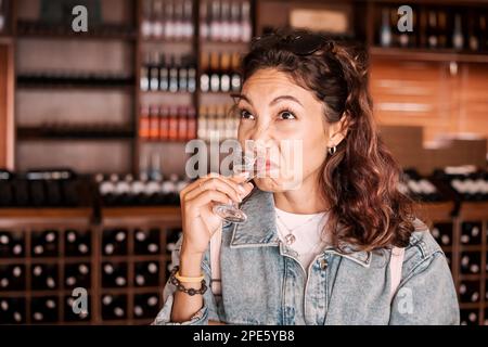 La ragazza annietta l'odore del vino e fa un volto con un'emozione di disgusto e dispiacere Foto Stock