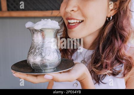 La ragazza beve un tradizionale latte fermentato kazako e asiatico dal latte di mare - koumose da una tazza d'argento con schiuma Foto Stock