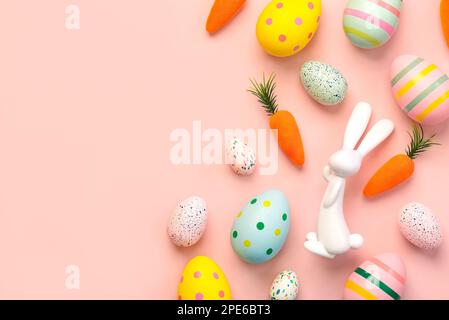 Composizione con uova di pasqua colorate, coniglietto di pasqua e carote con spazio copia per il testo su sfondo rosa Foto Stock