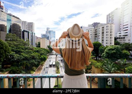 Turismo a San Paolo. Vista posteriore della bella ragazza viaggiatore che tiene il cappello godendo la vista del paesaggio urbano di Sao Paulo, Brasile. Foto Stock