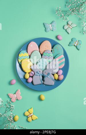 Banner pasquale su sfondo menta. Biscotti di pan di zenzero fatti in casa su un piatto blu, uova di Pasqua e biscotti a forma di coniglio e farfalla. EA Foto Stock