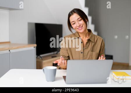 Studentessa asiatica che utilizza l'app per la comunicazione video a distanza, studia online, frequenta corsi mentre si soggiorna a casa. Ragazza che guarda lo schermo del notebook e gioisce Foto Stock